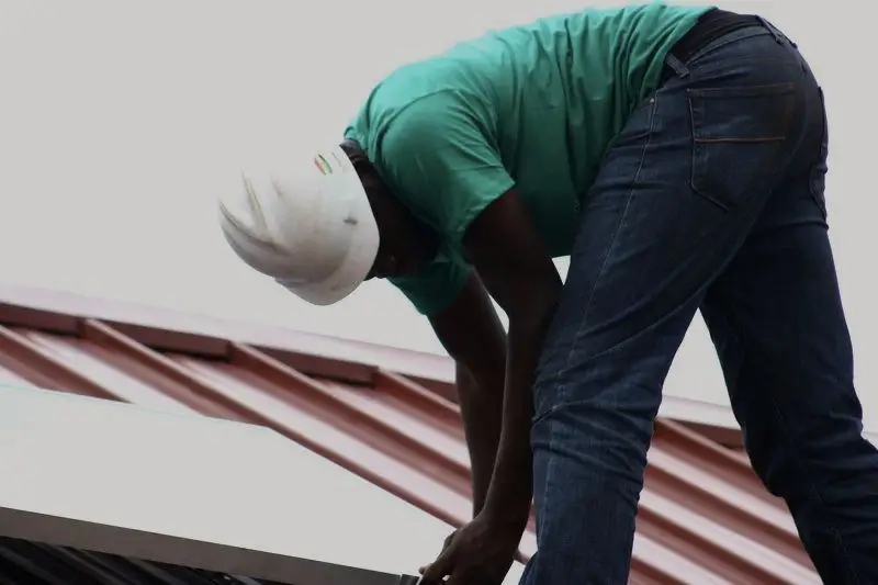 Technician in a hard hat bolting a solar module onto a corrugated roof